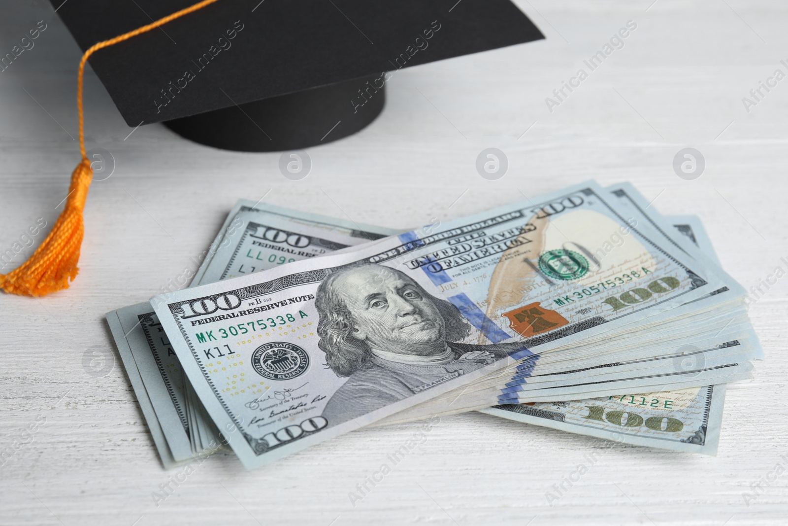 Photo of Dollar banknotes and student graduation hat on white wooden background. Tuition fees concept