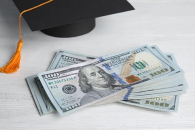 Photo of Dollar banknotes and student graduation hat on white wooden background. Tuition fees concept