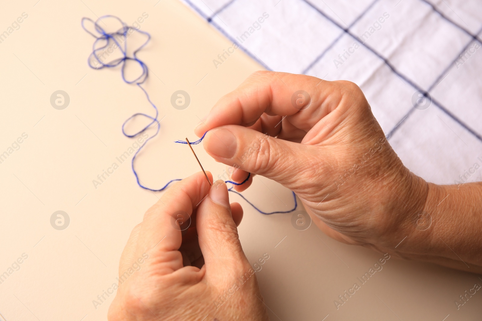 Photo of Closeup view of woman threading needle at beige table