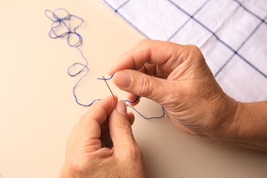 Photo of Closeup view of woman threading needle at beige table
