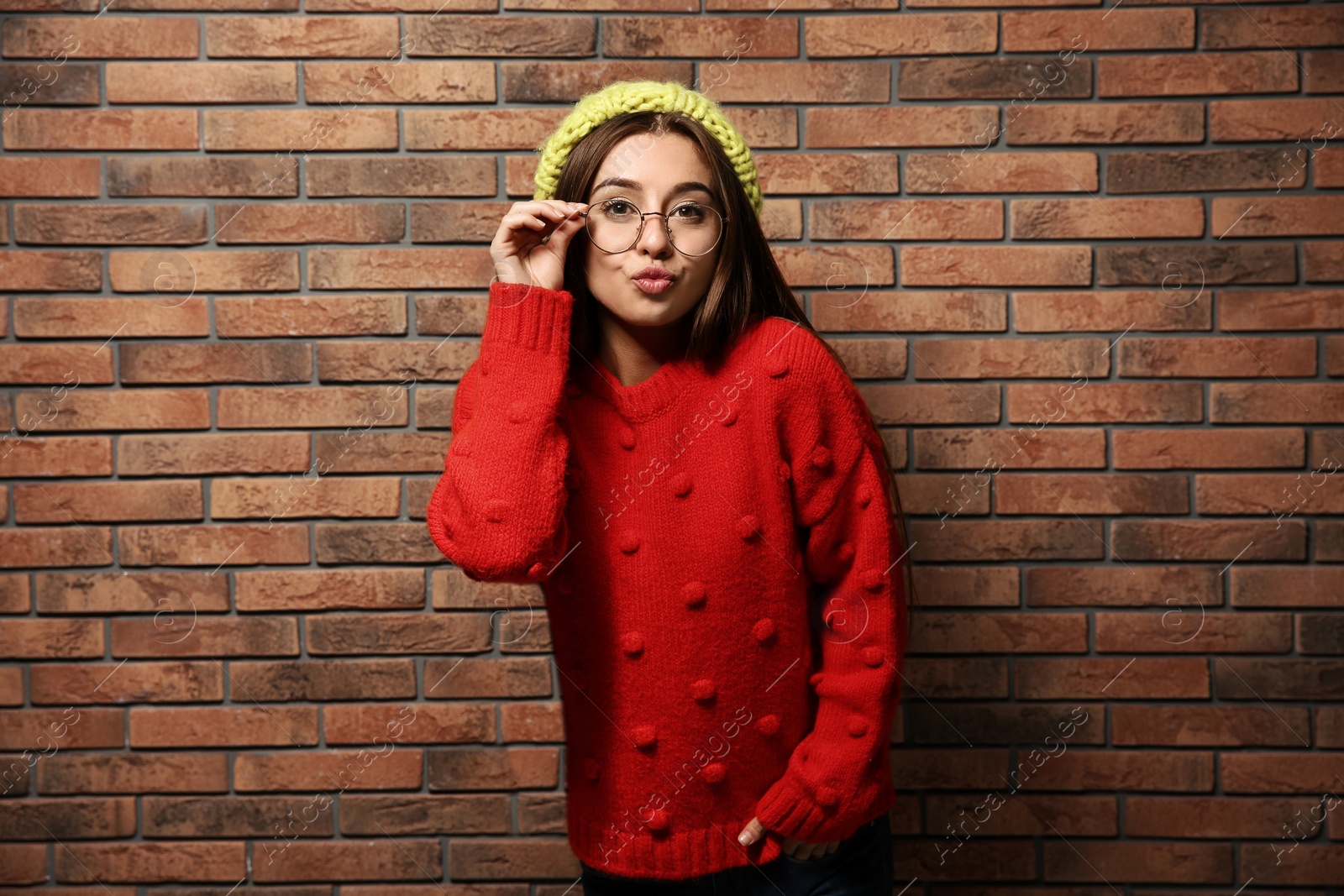 Photo of Beautiful young woman in warm sweater with hat near brick wall