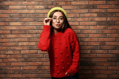 Photo of Beautiful young woman in warm sweater with hat near brick wall