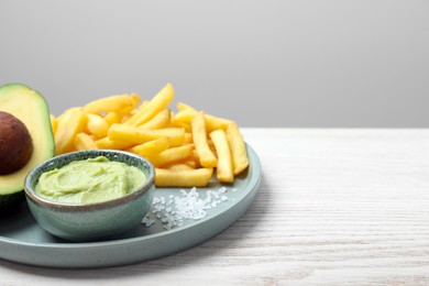 Plate with french fries, guacamole dip and avocado served on white wooden table, space for text