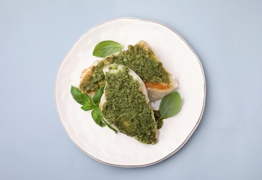 Delicious chicken breasts with pesto sauce and basil on light gray table, top view