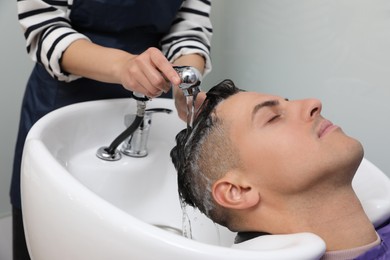 Photo of Professional hairdresser washing client's hair at sink indoors, closeup