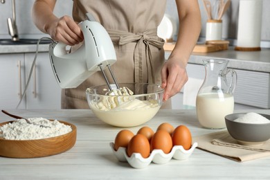 Photo of Woman whipping white cream with mixer at light grey table in kitchen, closeup