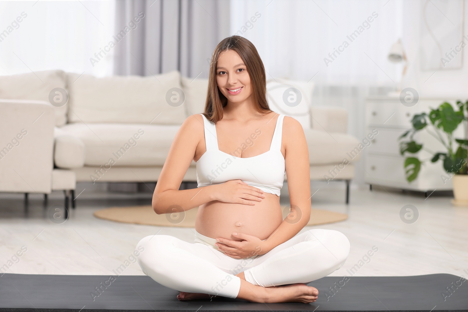 Photo of Beautiful pregnant woman sitting on yoga mat at home