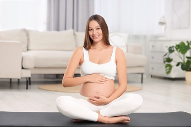 Beautiful pregnant woman sitting on yoga mat at home