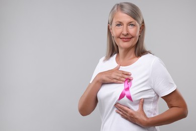 Beautiful senior woman with pink ribbon on light grey background, space for text. Breast cancer awareness