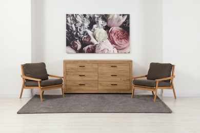 Stylish living room with wooden chest of drawers, armchairs and beautiful picture. Interior design