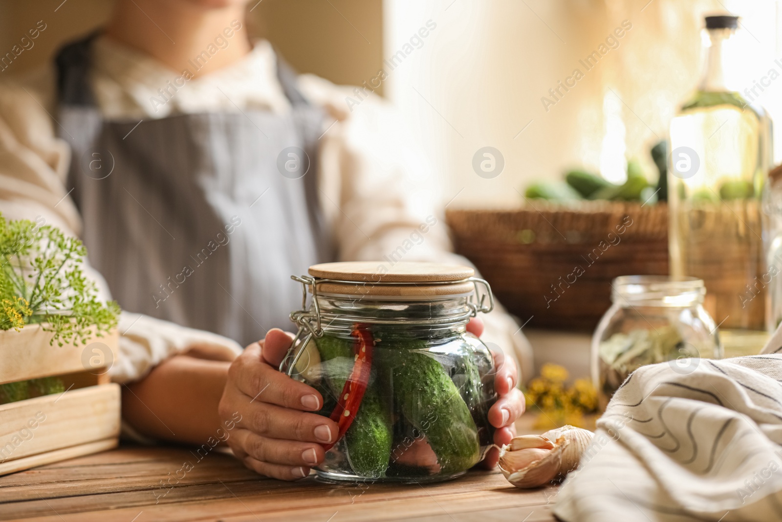 Photo of Woman holding glass jar of pickled cucumbers at wooden table, closeup