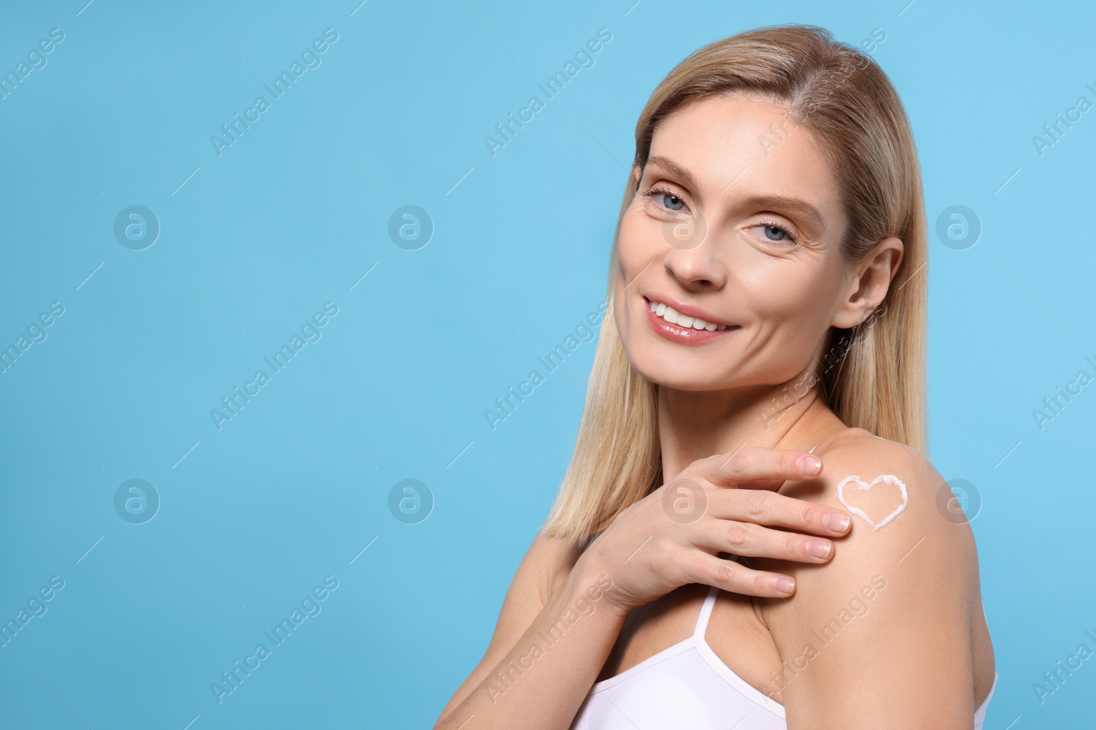 Photo of Woman with body cream onto her arm against light blue background, space for text