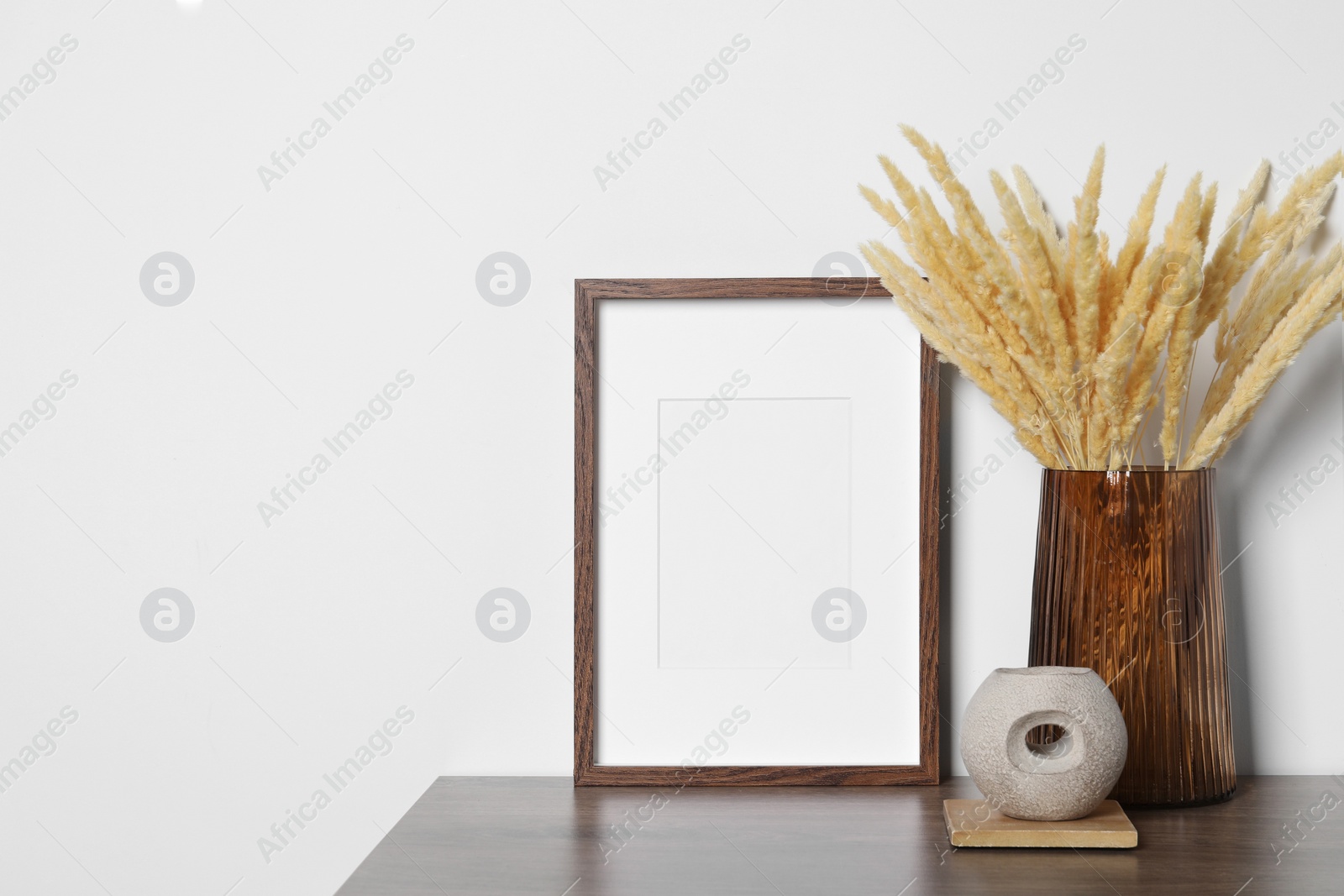 Photo of Empty photo frame and vase with dry decorative spikes on wooden table. Mockup for design