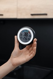 Photo of Woman holding digital hygrometer with thermometer at home, closeup