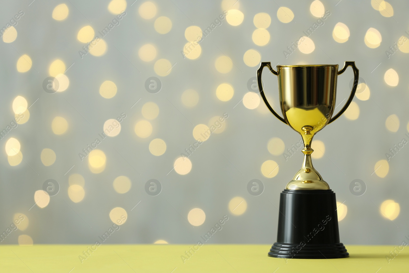 Photo of Golden trophy cup on table against blurred lights. Space for text