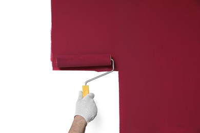 Photo of Man applying burgundy paint with roller brush on white wall, closeup
