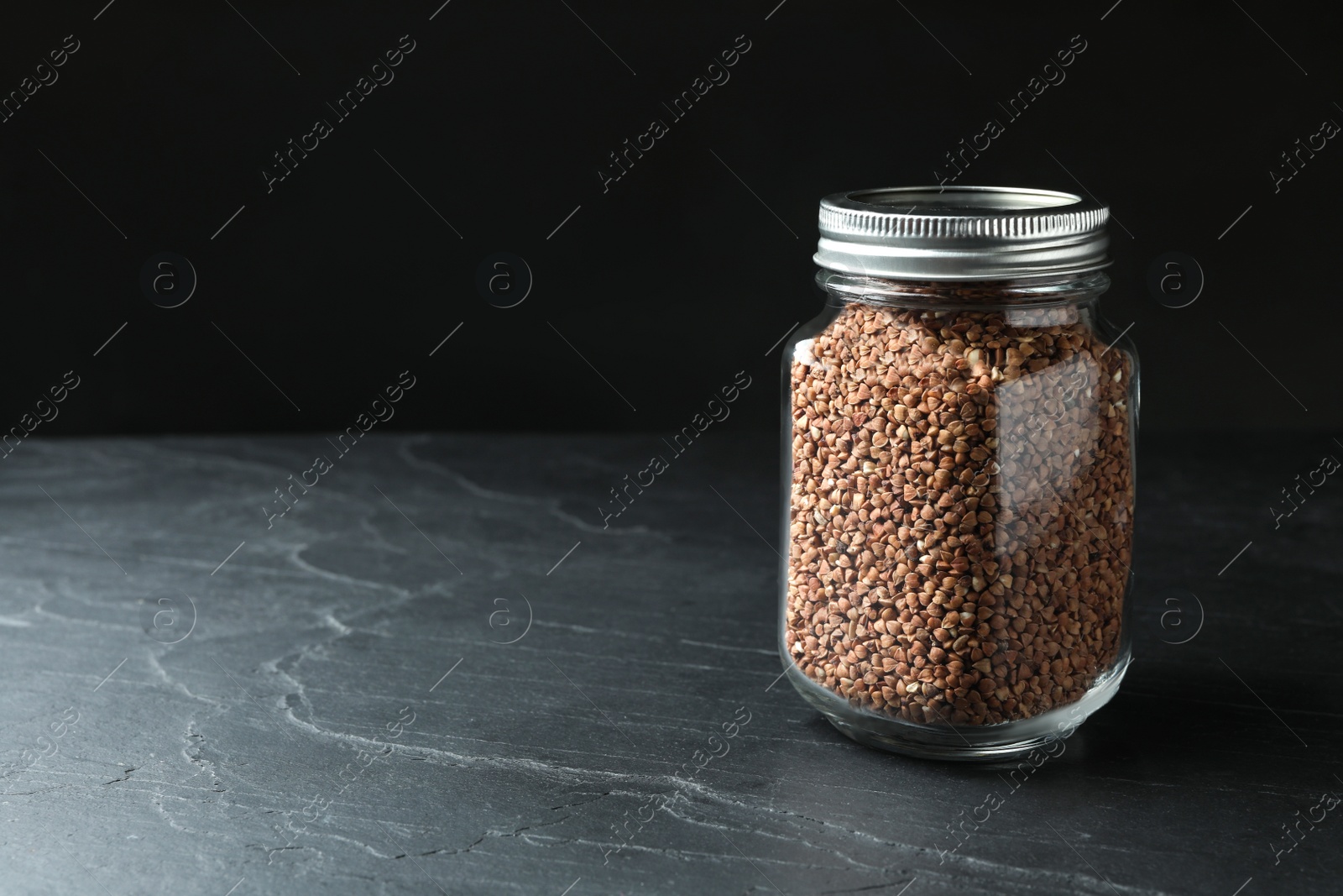 Photo of Buckwheat grains in jar on black table. Space for text