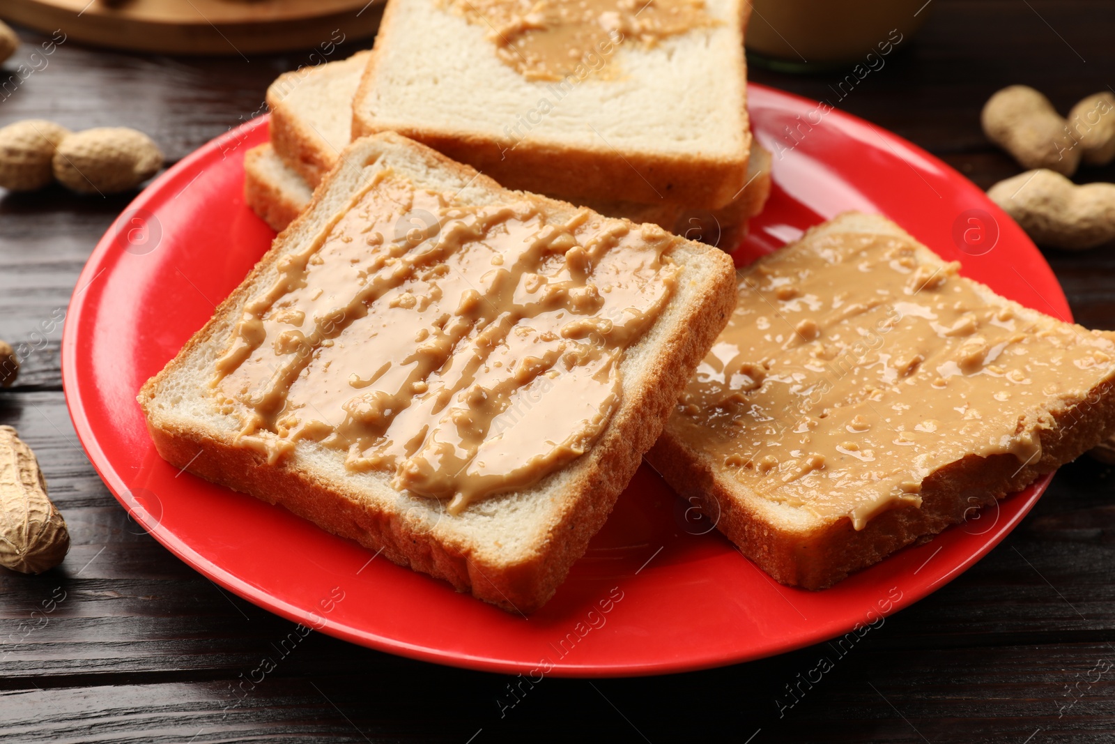 Photo of Delicious toasts with peanut butter on dark wooden table, closeup