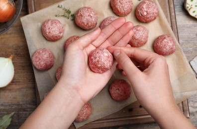 Photo of Woman making fresh raw meatballs at wooden table, top view