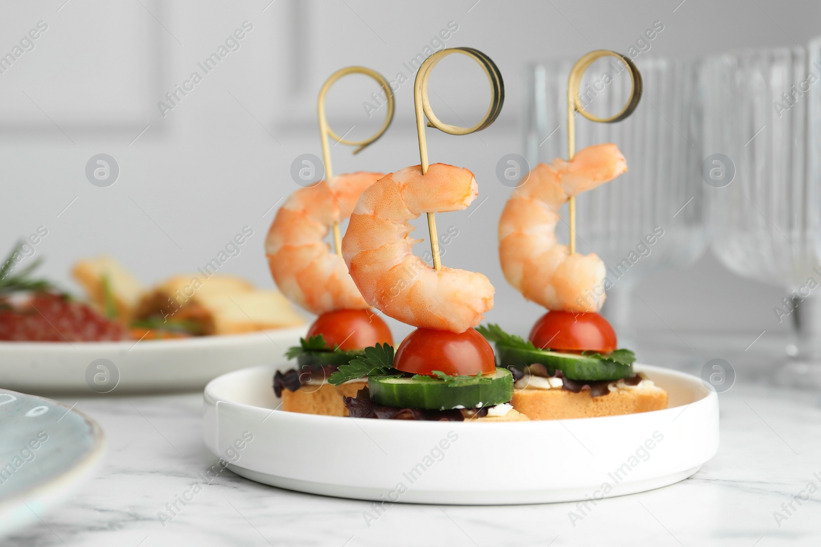 Photo of Tasty canapes with shrimps, cucumber, greens and tomatoes on white marble table, closeup