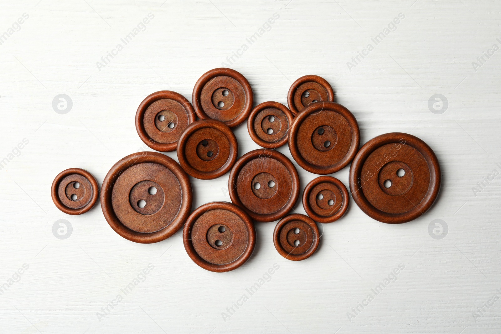 Photo of Many brown sewing buttons on white wooden background, flat lay