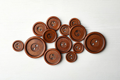 Photo of Many brown sewing buttons on white wooden background, flat lay