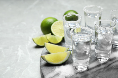 Photo of Mexican Tequila shots, lime slices and salt on grey marble table