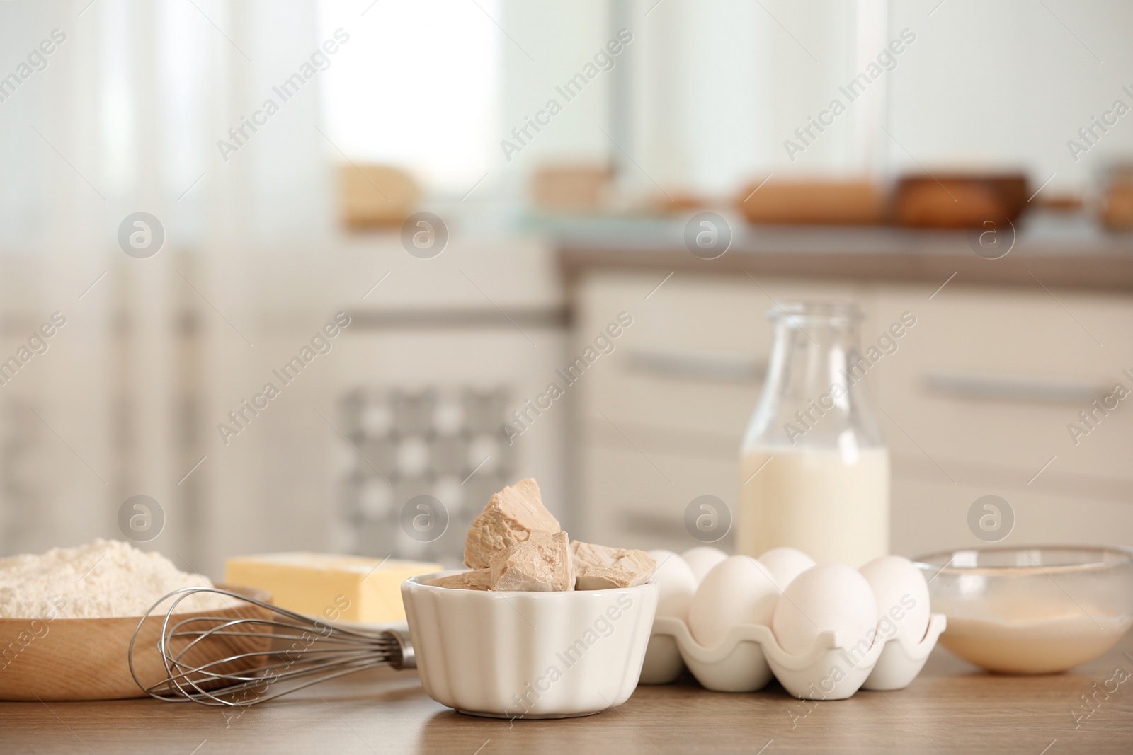 Photo of Pieces of compressed yeast and dough ingredients on wooden table indoors, space for text