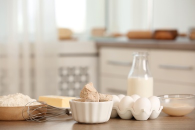 Pieces of compressed yeast and dough ingredients on wooden table indoors, space for text