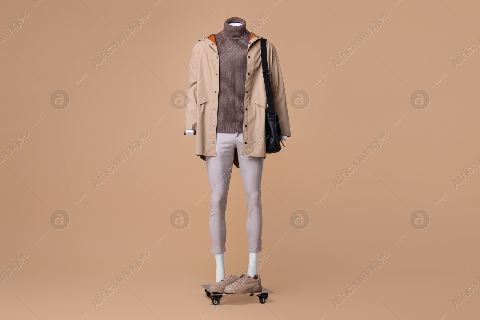 Photo of Male mannequin with bag dressed in stylish coat, turtleneck and pants on beige background