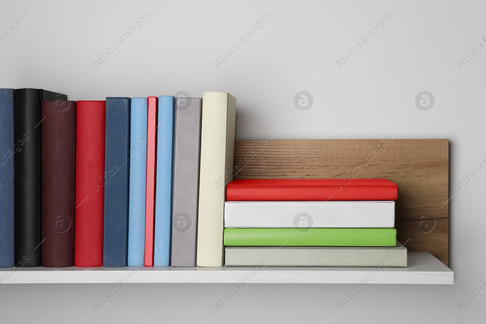 Photo of Many hardcover books on wooden shelf near white wall