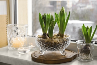 Photo of Beautiful bulbous plants and candles on windowsill indoors. Spring time