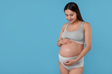 Photo of Beautiful pregnant woman in comfortable maternity underwear on light blue background, space for text