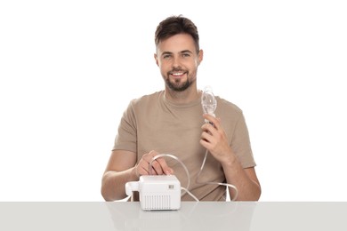 Man turning on nebulizer for inhalation at table against white background
