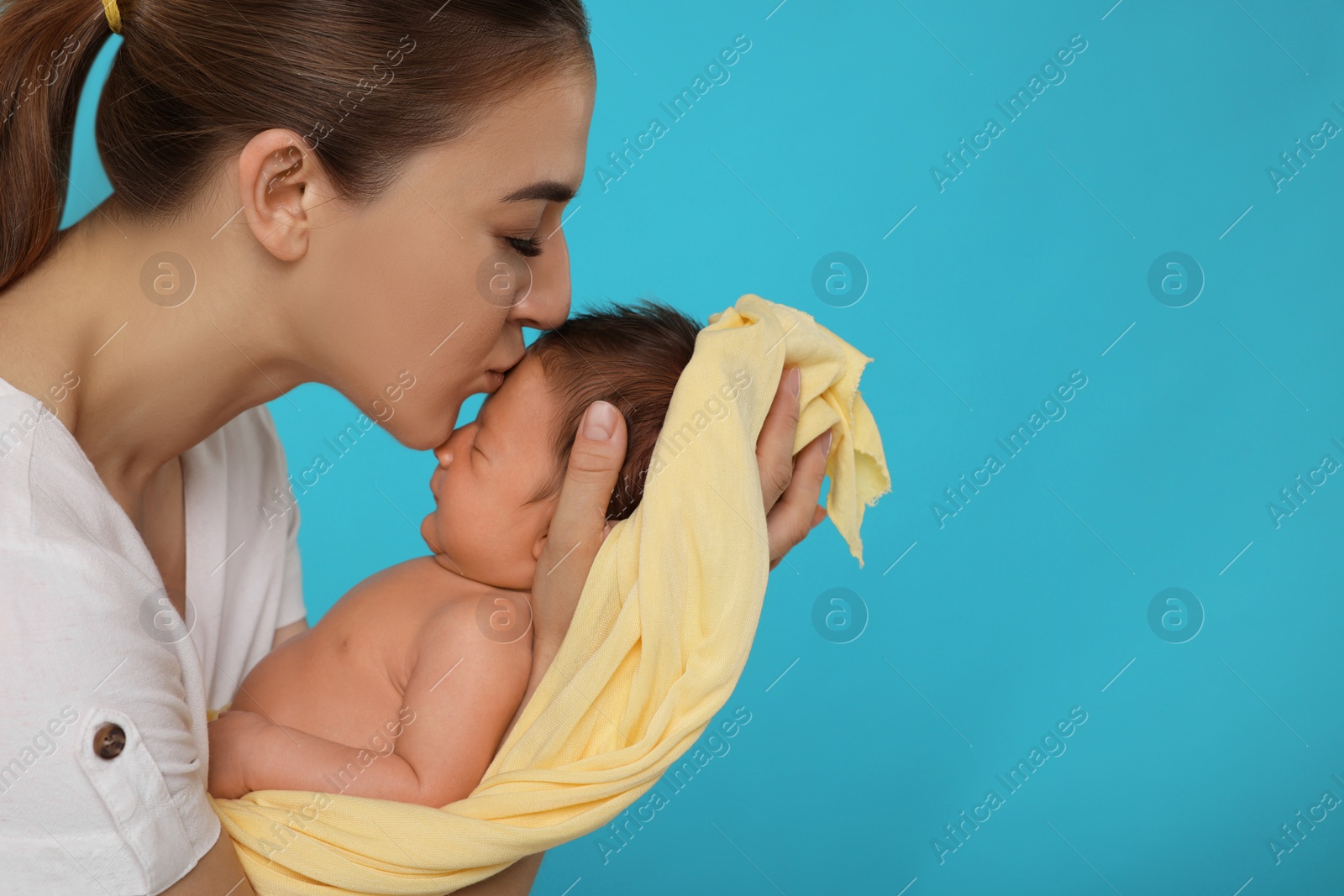 Photo of Mother kissing her cute newborn baby on light blue background, closeup. Space for text