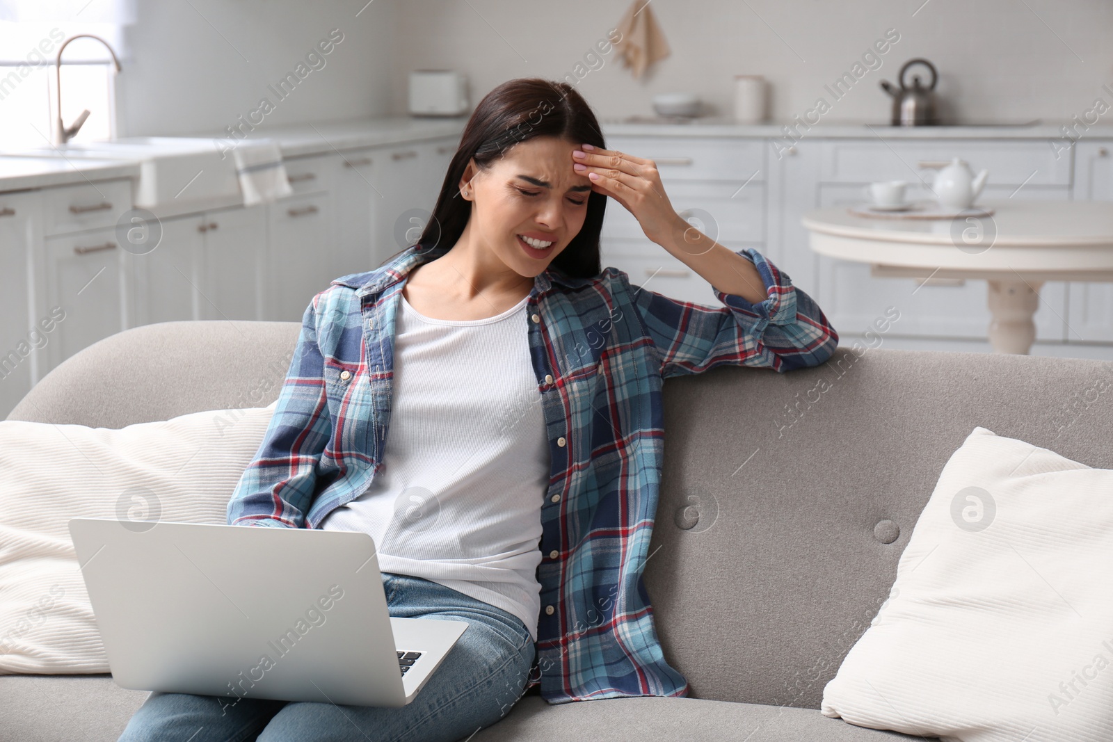 Photo of Young woman with laptop suffering from migraine at home