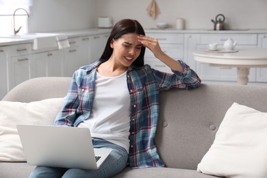 Photo of Young woman with laptop suffering from migraine at home