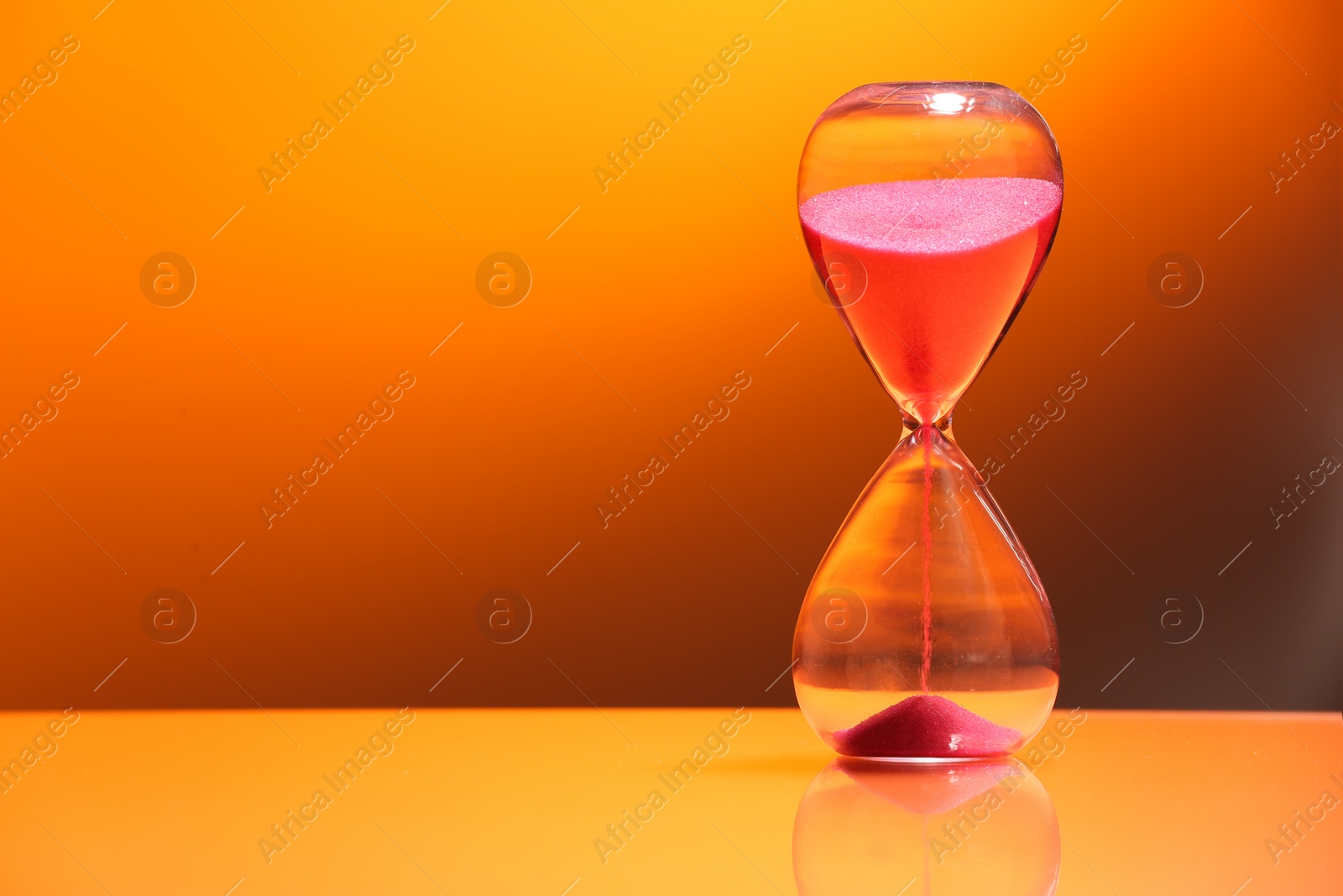 Photo of Hourglass with flowing sand on color background. Space for text