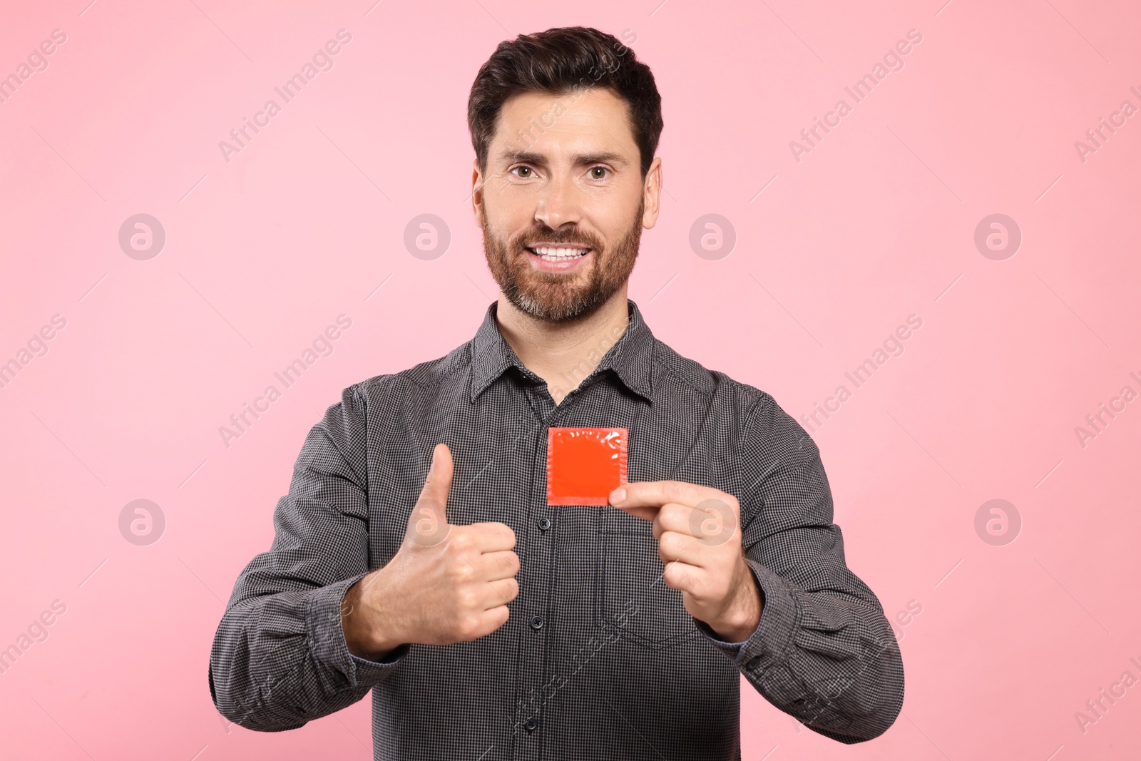 Photo of Happy man with condom showing thumb up on pink background. Safe sex