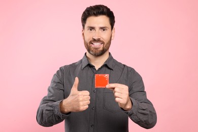 Photo of Happy man with condom showing thumb up on pink background. Safe sex