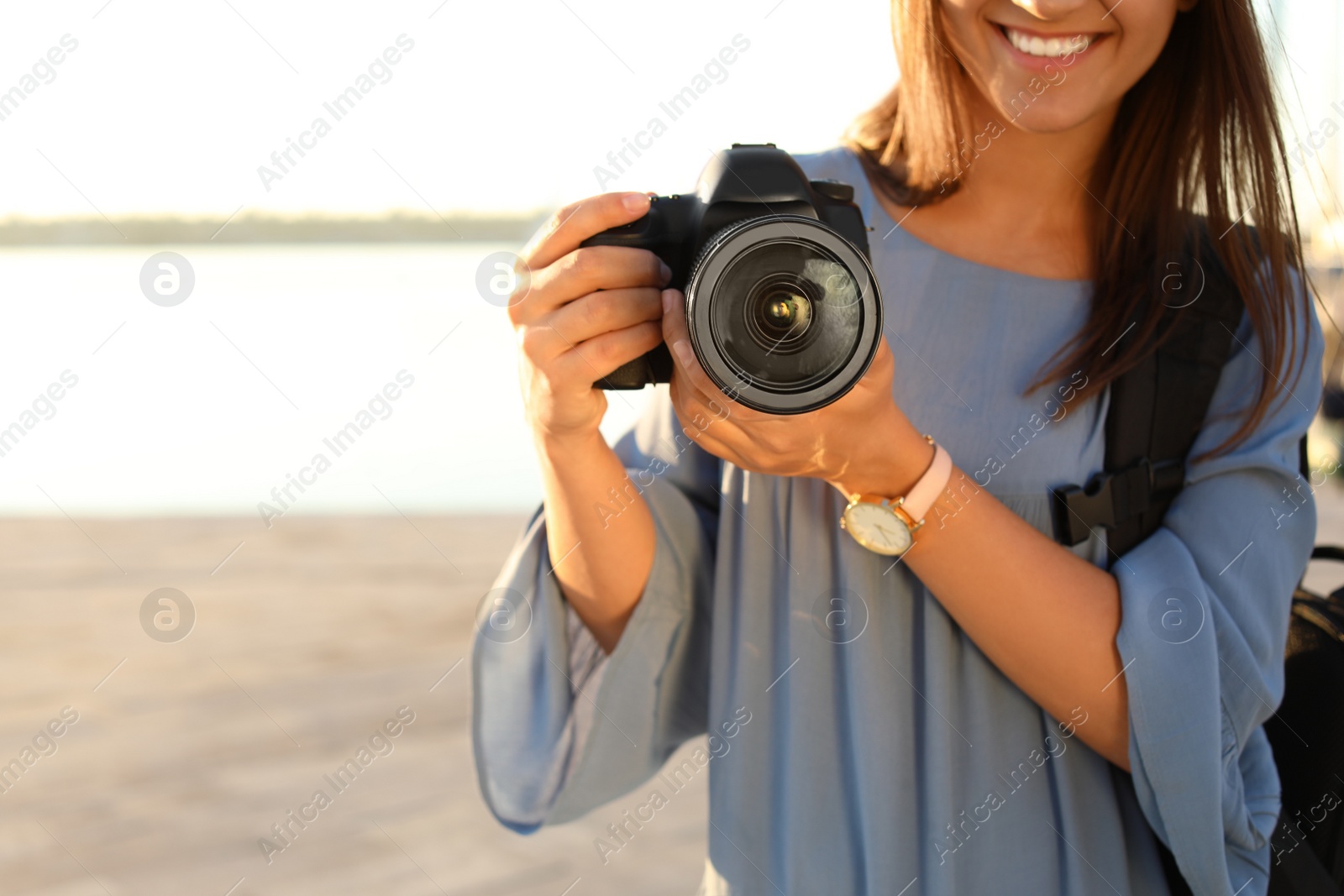 Photo of Young female photographer holding professional camera at pier, closeup. Space for text