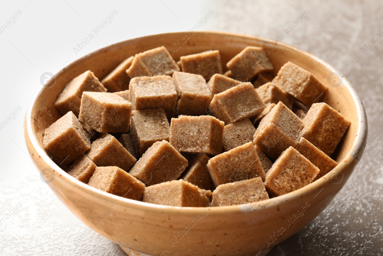 Photo of Bowl with cubes of brown sugar on table, closeup