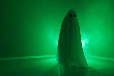 Photo of Creepy ghost. Woman covered with sheet in green light, space for text