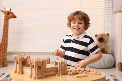 Cute little boy playing with wooden construction set at table in room. Child's toy