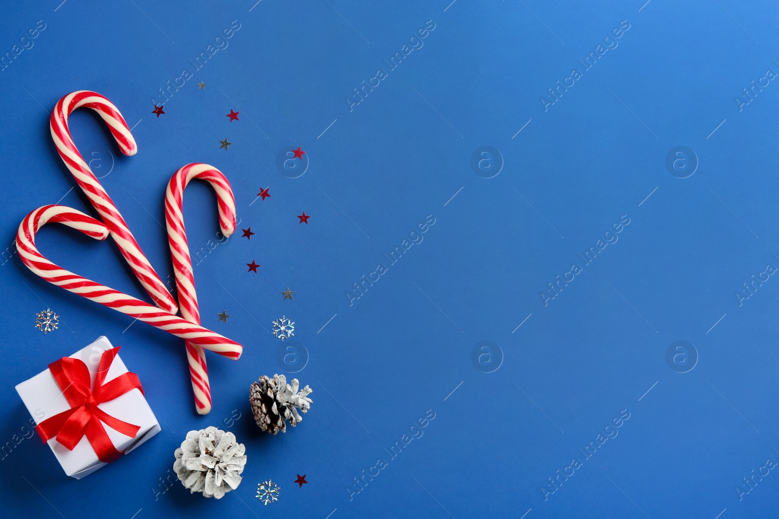 Photo of Candy canes, Christmas gift and pine cones on blue background, flat lay. Space for text