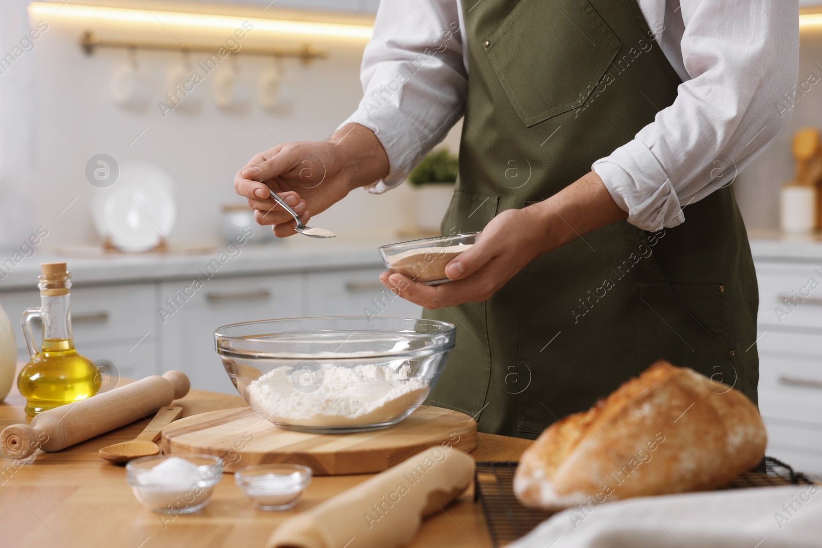 Photo of Making bread. Man putting dry yeast into bowl with flour at wooden table in kitchen, closeup