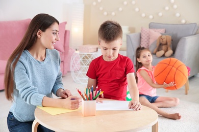 Photo of Cute little child drawing at table with young woman in playing room