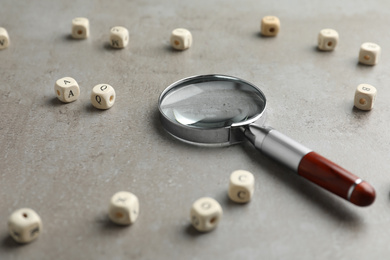 Photo of Magnifier glass and cubes with letters on light grey stone background, closeup. Find keywords concept