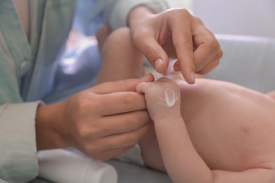 Photo of Mother applying moisturizing cream onto baby`s hand on changing table, closeup