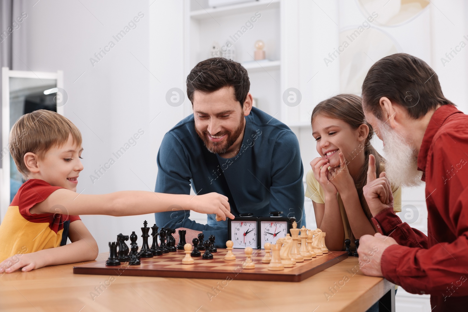 Photo of Family playing chess together at table in room